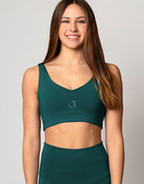 Woman wearing a green sports bra and leggings on a plain background