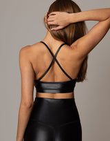 Person wearing a black shiny sports bra and leggings against a neutral background