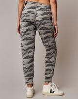 Person wearing gray camouflage jogger pants with white sneakers on a plain background