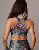 Rear view of a woman wearing a matching floral sports bra and high-waisted leggings set against a solid gray studio background.