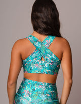 Rear view of a woman wearing a matching turquoise floral sports bra and high-waisted leggings set against a solid gray studio background.
