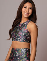 A woman modeling a matching two-piece activewear set featuring a dark gray floral print with pink, green, and white botanical details, set against a solid gray studio background.