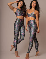 Two women modeling matching floral print activewear sets consisting of sports bras and high-waisted leggings, posed against a solid beige studio background.