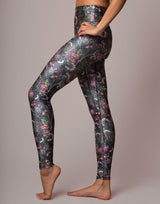 A model wearing high-waisted leggings with a dark floral and bird pattern, shown from the waist down against a solid neutral studio background.