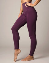 woman wearing eggplant purple colored leggings on grey background
