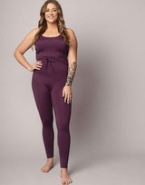 woman wearing eggplant purple colored tank top and leggings on grey background