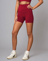 Person wearing red high-waisted shorts and white sneakers on a gray background