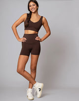 woman wearing chocolate brown colored shorts and v neck crop top on grey background
