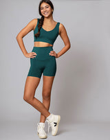 Woman wearing a green athletic outfit with white sneakers on a gray background