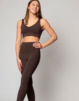 woman wearing chocolate brown colored legging and v neck crop top on grey background