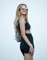 Woman wearing a black athletic outfit with sunglasses on a light gray background