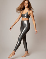 Woman wearing metallic silver leggings and sports bra on a plain background