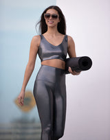 Woman in metallic silver athletic wear holding a yoga mat against a blurred outdoor background