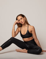Woman wearing a black sports bra and leggings sitting on a light gray background
