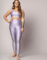 woman wearing v neck crop top and legging set with mermaid pattern of lavender purple colored sparkling fish scales on grey background