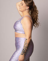 woman wearing v neck crop top with mermaid pattern of lavender purple colored sparkling fish scales on grey background