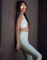 woman wearing crop top and legging with mermaid pattern of mint colored sparkling fish scales on dark background