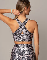 Woman wearing a black and white floral sports bra and leggings on a neutral background