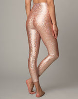 woman wearing legging with mermaid pattern of peach colored sparkling fish scales on grey background