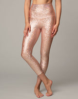 woman wearing legging with mermaid pattern of peach colored sparkling fish scales on grey background