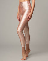 woman wearing legging with mermaid pattern of peach colored sparkling fish scales on grey background