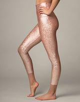 woman wearing legging with mermaid pattern of peach colored sparkling fish scales on grey background