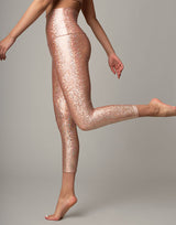 woman wearing legging with mermaid pattern of peach colored sparkling fish scales on grey background