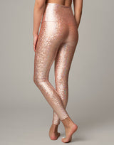 woman wearing legging with mermaid pattern of peach colored sparkling fish scales on grey background