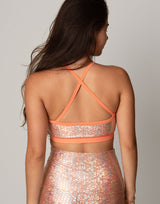 Woman wearing a sparkly two-piece outfit with an orange trim against a plain background