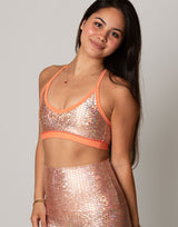 Woman wearing a sparkly two-piece outfit with an orange trim against a plain background