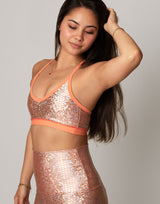 Woman wearing a sparkly two-piece outfit with an orange trim against a plain background