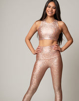 woman wearing crop top with mermaid pattern of peach colored sparkling fish scales on grey background