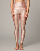 woman wearing legging with mermaid pattern of peach colored sparkling fish scales on grey background