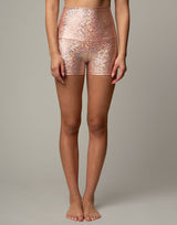 woman wearing shorts with mermaid pattern of peach colored sparkling fish scales on grey background