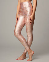 woman wearing legging with mermaid pattern of peach colored sparkling fish scales on grey background