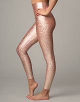 woman wearing legging with mermaid pattern of peach colored sparkling fish scales on grey background