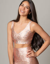 woman wearing v neck crop top with mermaid pattern of peach colored sparkling fish scales on grey background