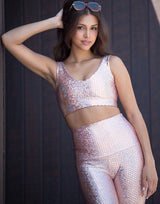 woman wearing v neck crop top with mermaid pattern of peach colored sparkling fish scales on dark background