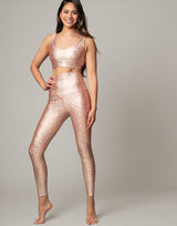 woman wearing legging with mermaid pattern of peach colored sparkling fish scales on grey background