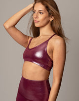 Woman wearing a shiny maroon sports bra and leggings against a neutral background