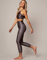 Woman wearing a leopard print sports bra and leggings on a plain background