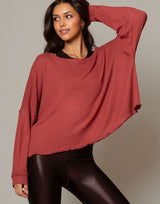 woman wearing oversized waffle knit long sleeve top in papaya red orange on grey background