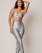 Woman wearing a snakeskin pattern sports bra and leggings on a plain background