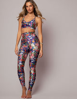 Woman wearing a colorful floral sports bra and leggings set on a gray background