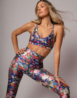 Woman wearing a colorful floral sports bra and leggings set on a gray background