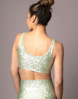 woman wearing v neck crop top with mermaid pattern of mint green colored sparkling fish scales on grey background