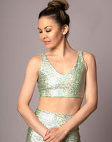 woman wearing v neck crop top with mermaid pattern of mint green colored sparkling fish scales on grey background