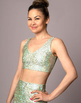 woman wearing v neck crop top with mermaid pattern of mint green colored sparkling fish scales on grey background