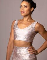 woman wearing v neck crop top with mermaid pattern of pink colored sparkling fish scales on grey background