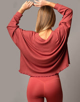 woman wearing oversized waffle knit long sleeve top in papaya red orange on grey background